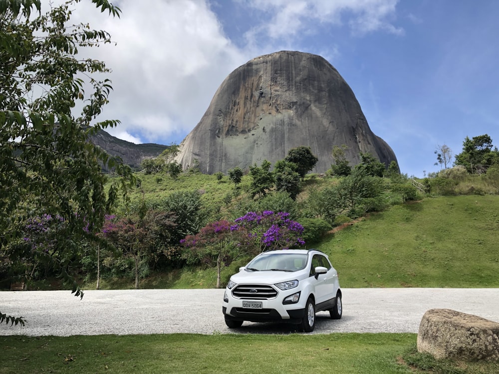 white suv parked near green grass and brown mountain during daytime