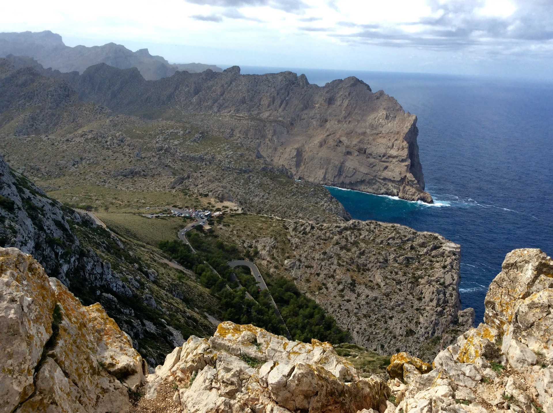 A panoramic view of a rugged coastline under a dramatic sky, where deep blue sea meets jagged cliffs.