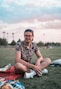 man in black and white floral button up shirt sitting on green grass field during daytime