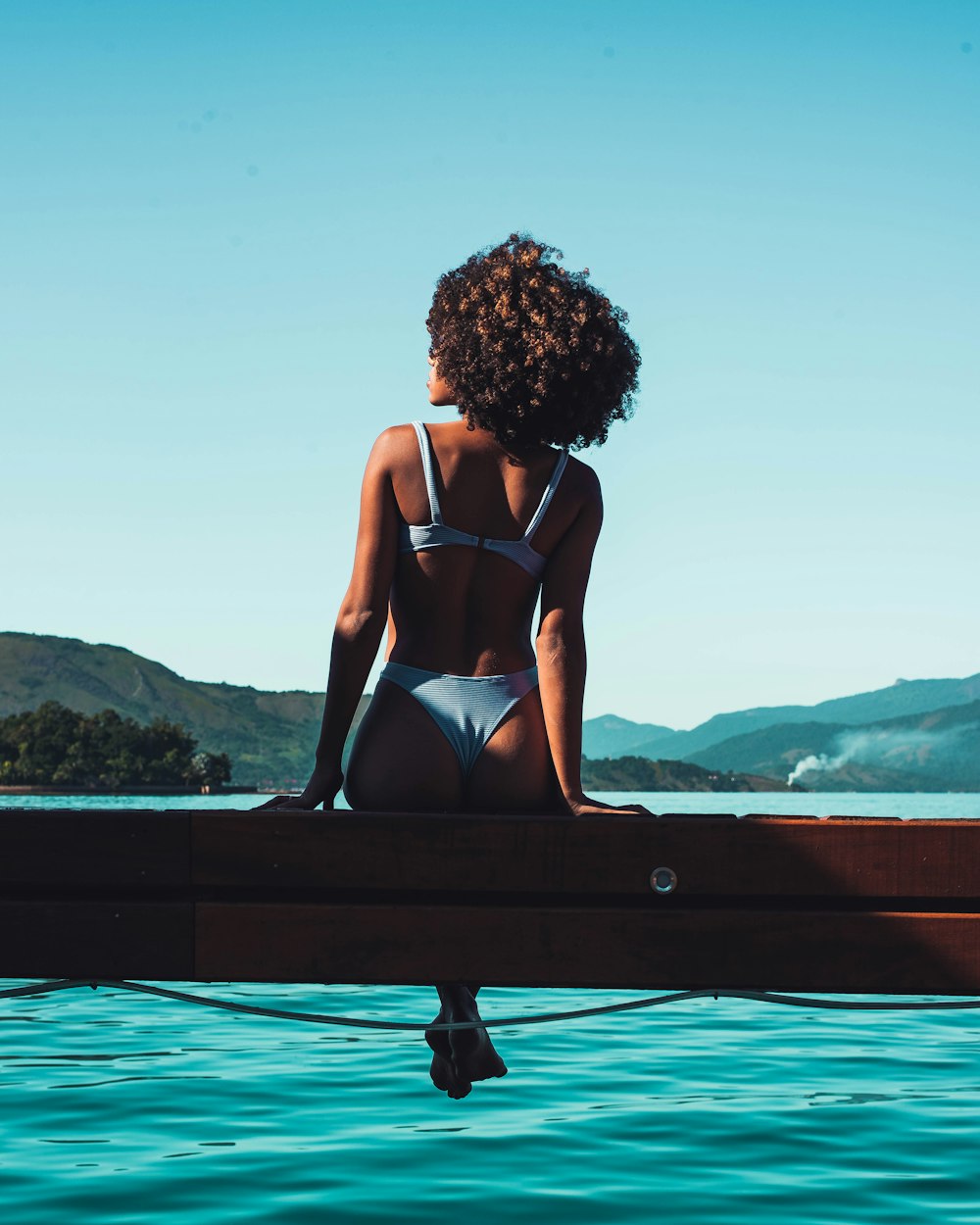 woman in black bikini sitting on black wooden bench during daytime