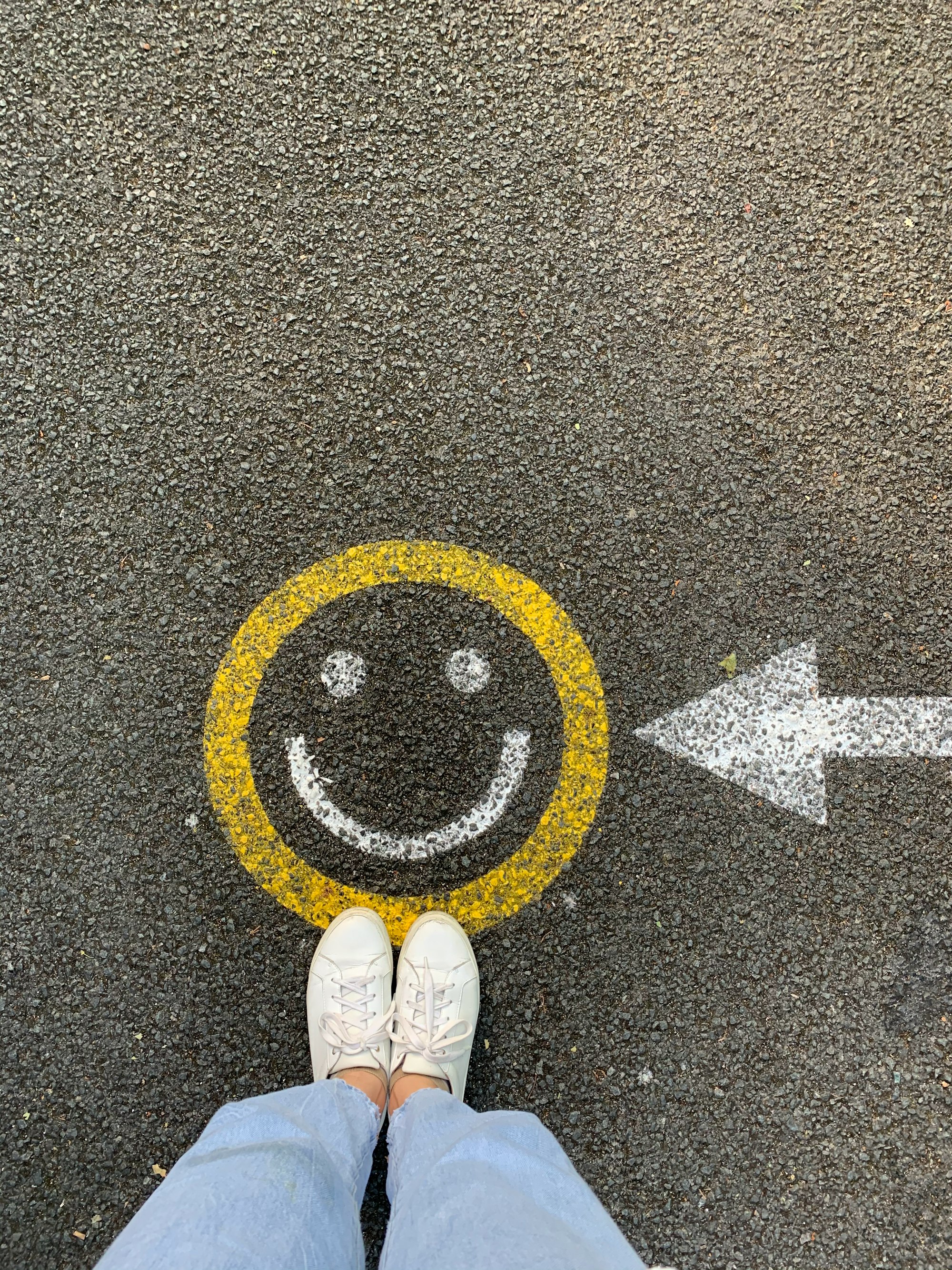 Person looking down at a happy face drawn on pavement - wornbee.com