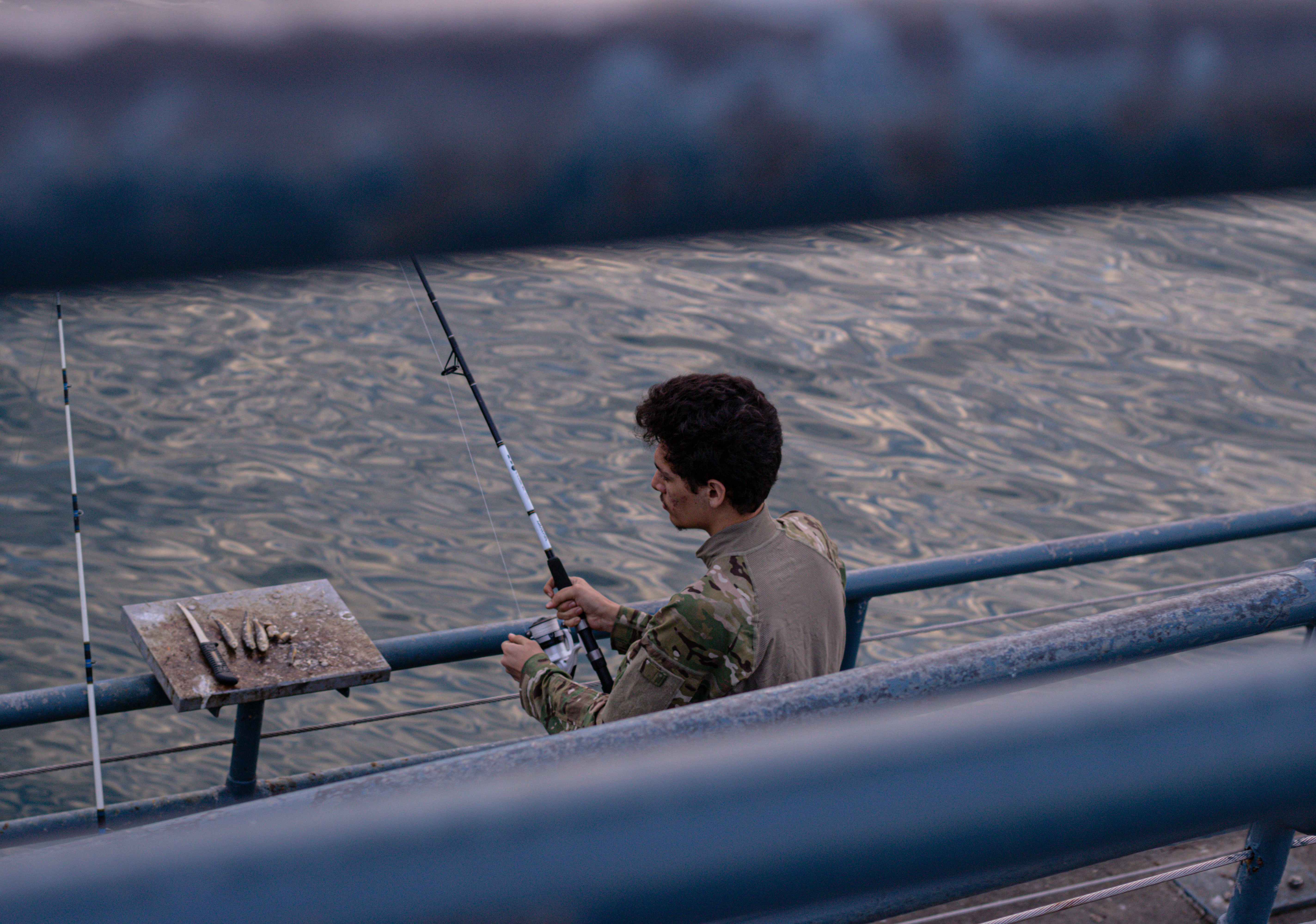 man in green jacket sitting on bench holding fishing rod during daytime