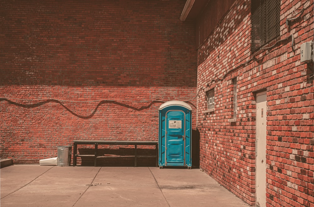 blue trash bin beside brown brick wall