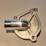 A close-up view of a shiny, metallic machined object with a cylindrical protrusion and intricate patterns. The object has a reflective surface, and the background appears to be a plain, light-colored surface.