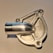 A close-up view of a shiny, metallic machined object with a cylindrical protrusion and intricate patterns. The object has a reflective surface, and the background appears to be a plain, light-colored surface.