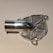 A metallic, intricately machined component with a tubular protrusion and detailed geometric patterns on its surface, likely a part for mechanical or industrial use.