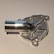 A metallic, intricately machined component with a tubular protrusion and detailed geometric patterns on its surface, likely a part for mechanical or industrial use.