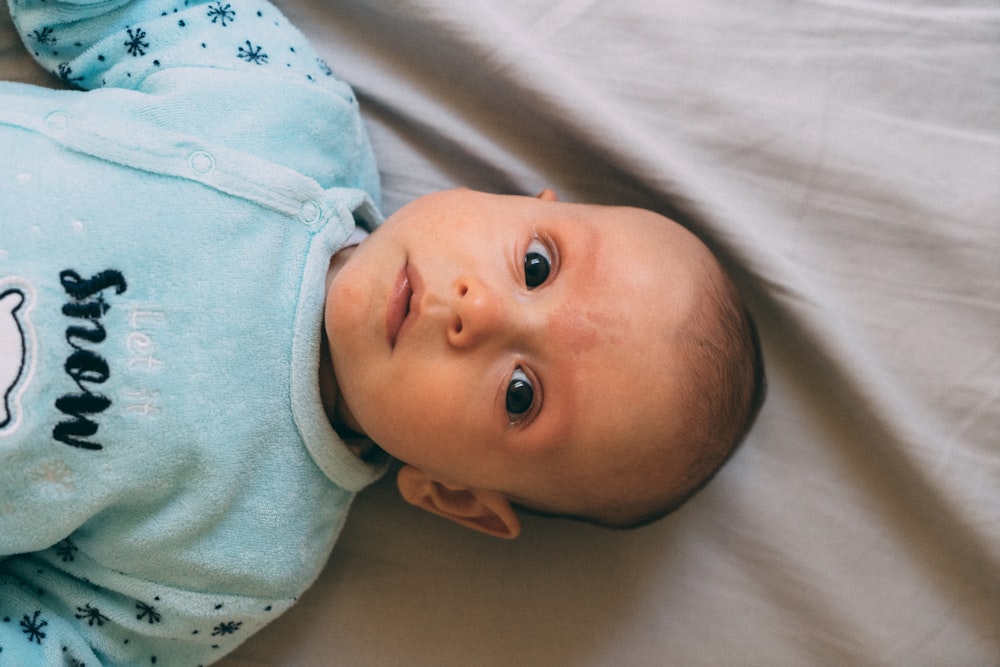 흰색 직물에 누워 있는 파란색 옷을 입은 아기