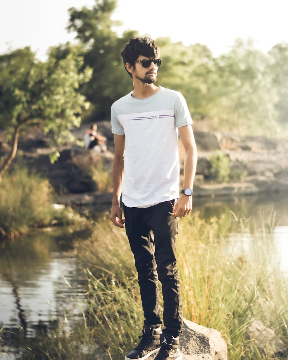 man in white crew neck t-shirt and black pants standing near river during daytime