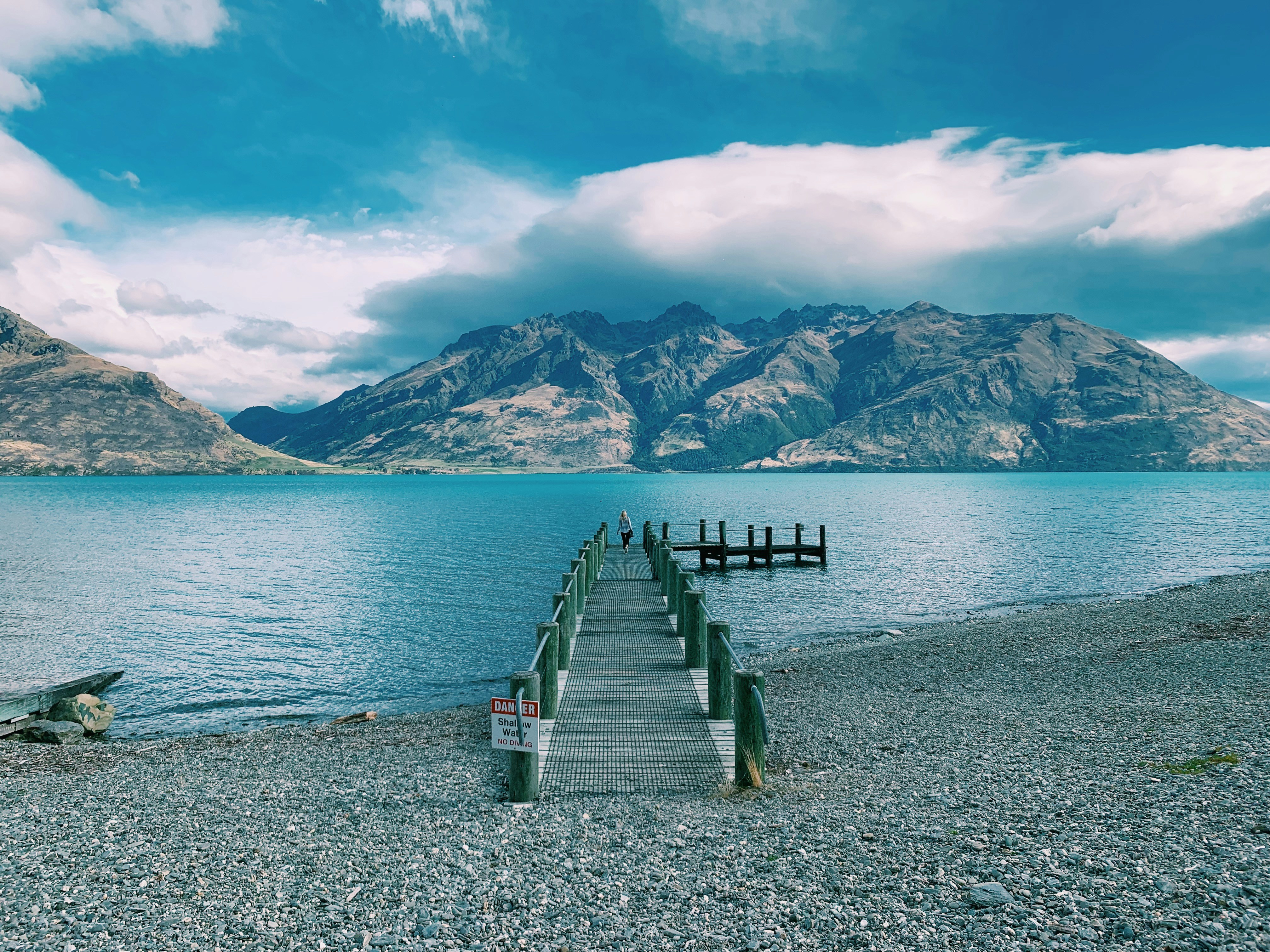 brown wooden dock on sea near mountain under blue sky during daytime
