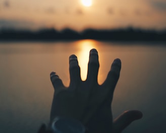 a persons hand reaching out over water during sunset