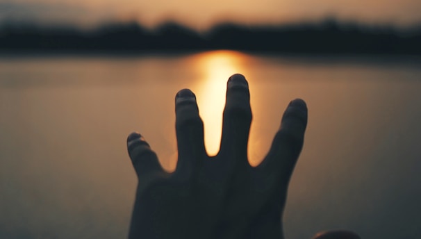 a persons hand reaching out over water during sunset