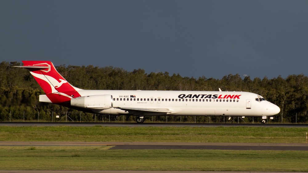 white and red passenger plane on green grass field under blue sky during daytime