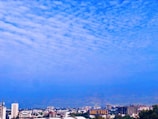 A cityscape with several buildings of varying heights, including a tall structure with the word 'METRO' prominently displayed. The sky is filled with scattered, fluffy clouds and has a gradient of blue hues.