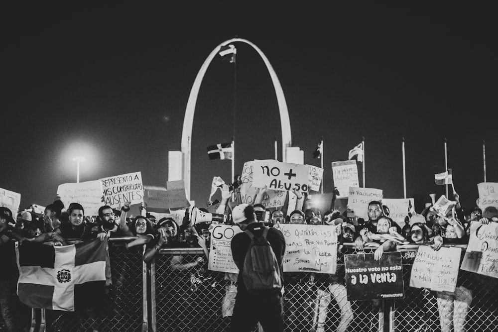 grayscale photo of people standing near fence