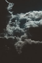 Dark, dramatic clouds with hints of moonlight create a moody, atmospheric scene. The contrast between light and shadows suggests an impending storm or nightfall.