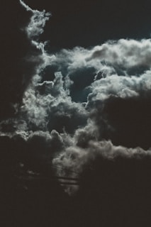 Dark, dramatic clouds with hints of moonlight create a moody, atmospheric scene. The contrast between light and shadows suggests an impending storm or nightfall.