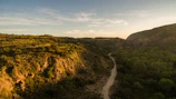 A winding hiking trail through lush green hills bathed in warm sunlight.