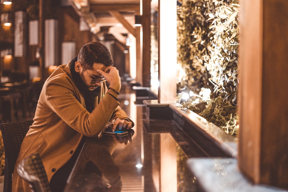 man in brown jacket sitting on brown wooden bench