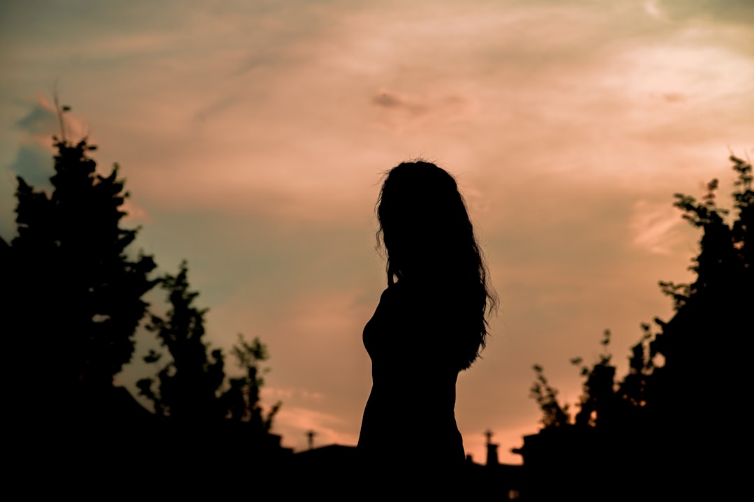 silhouette of woman standing near tree during sunset