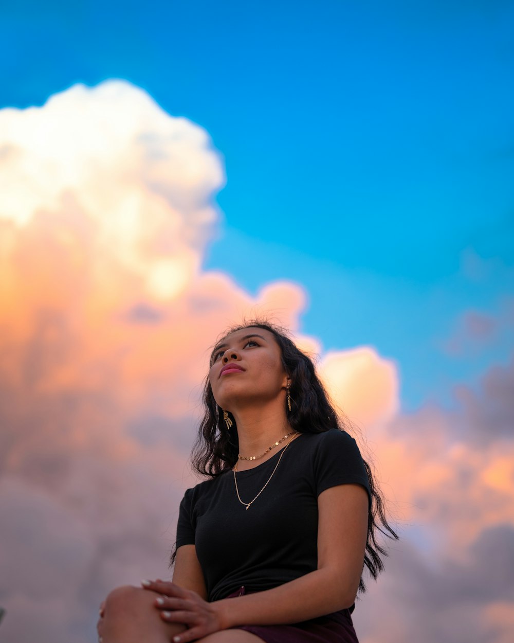 a woman sitting on a ledge looking up into the sky