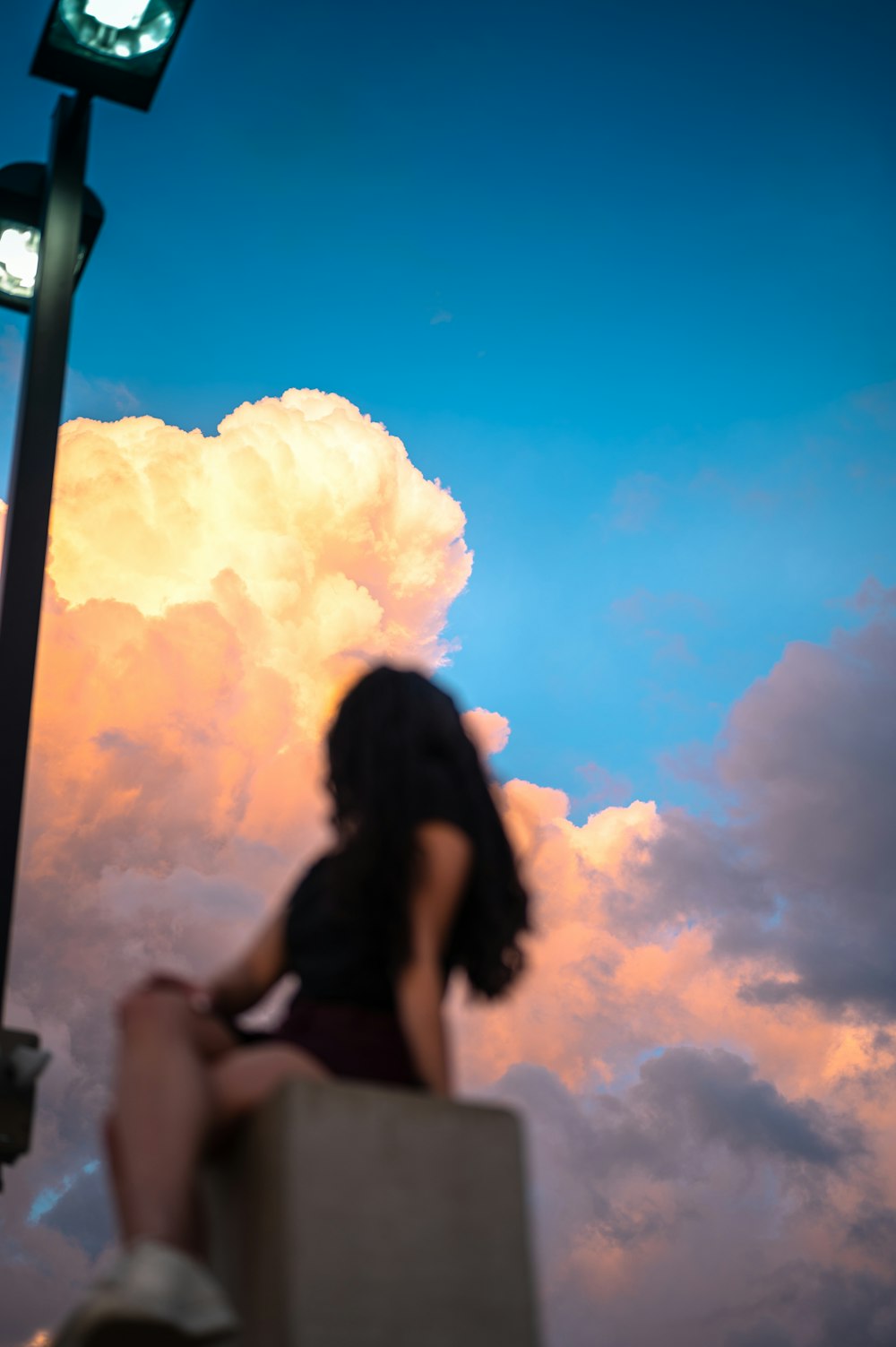 Mujer en camiseta sin mangas negra bajo el cielo azul y nubes blancas durante el día