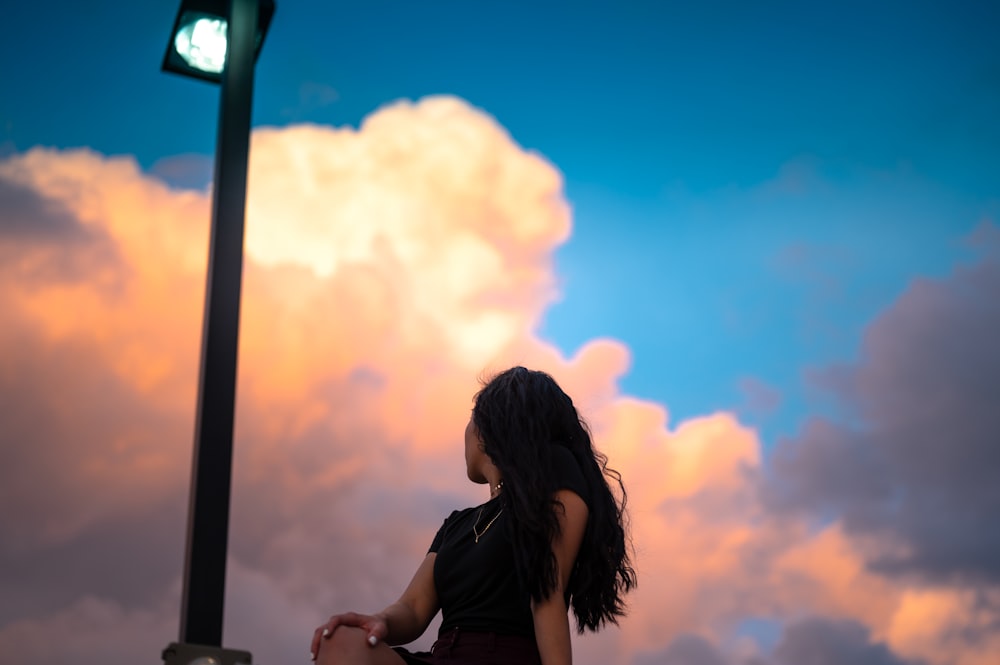 Mujer en camisa negra de pie y sonriendo durante la puesta del sol