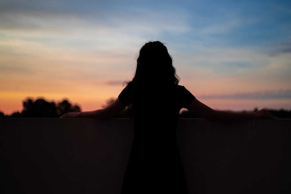 silhouette of woman standing on top of building during sunset