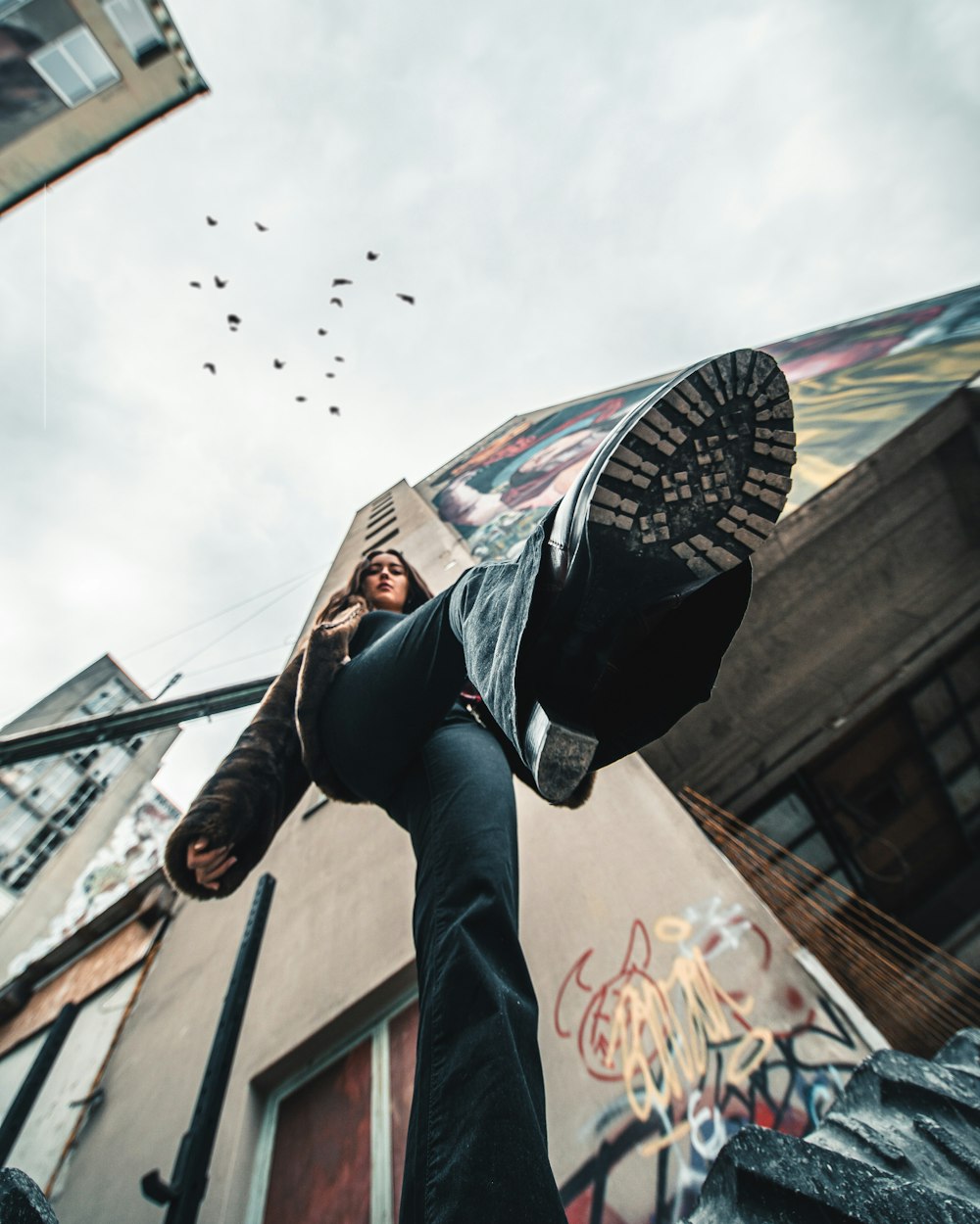 man in black jacket and blue denim jeans jumping on the building during daytime