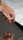 A hand with red painted nails is poised above an object with a reflective surface, creating a clear reflection of the fingers. The focus is on the well-groomed nails and the smooth skin of the hand set against a soft background.