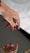A hand with red painted nails is poised above an object with a reflective surface, creating a clear reflection of the fingers. The focus is on the well-groomed nails and the smooth skin of the hand set against a soft background.