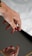 A hand with red painted nails is poised above an object with a reflective surface, creating a clear reflection of the fingers. The focus is on the well-groomed nails and the smooth skin of the hand set against a soft background.