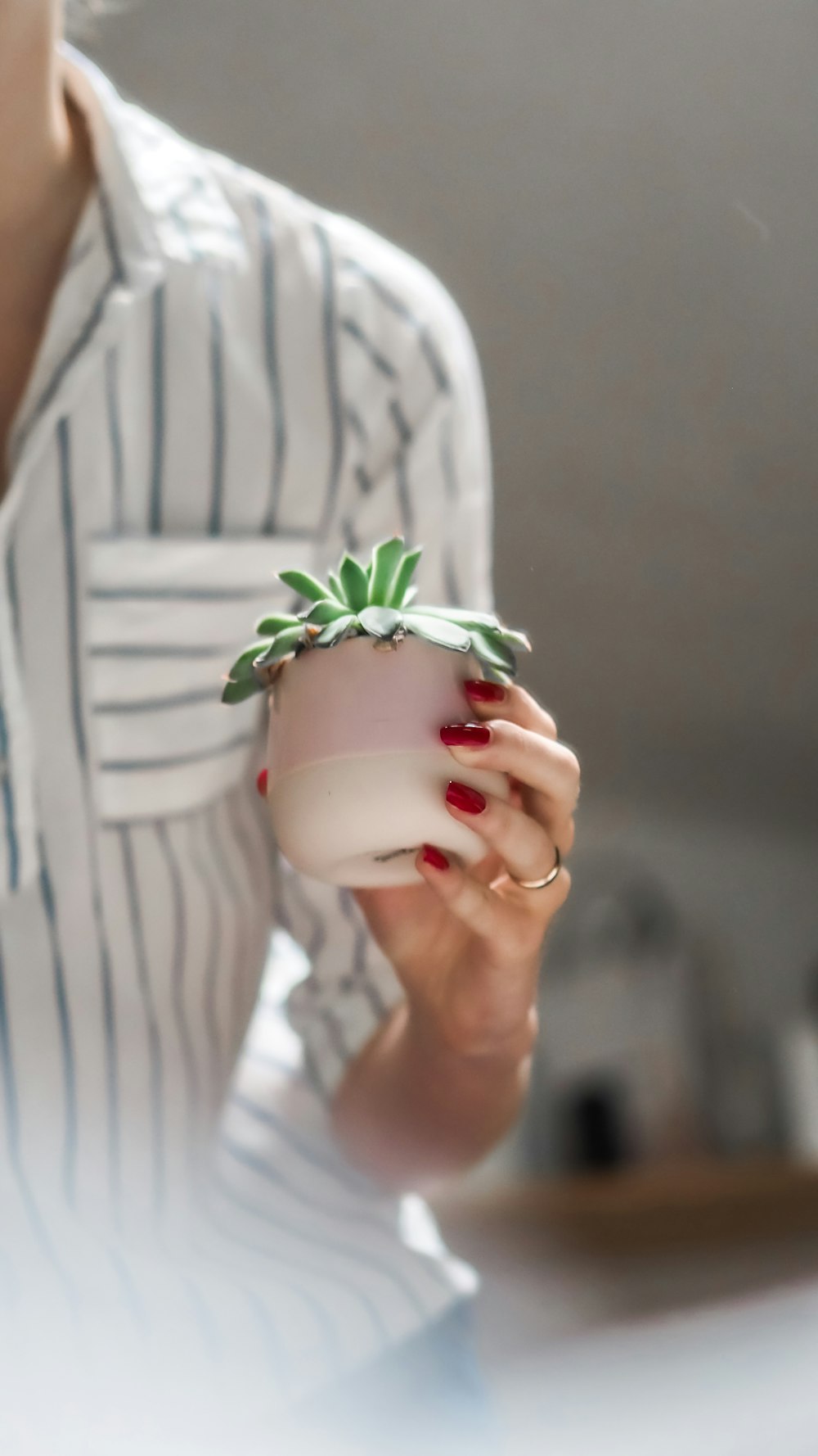 woman in white and gray stripe dress holding white ceramic mug with green plant