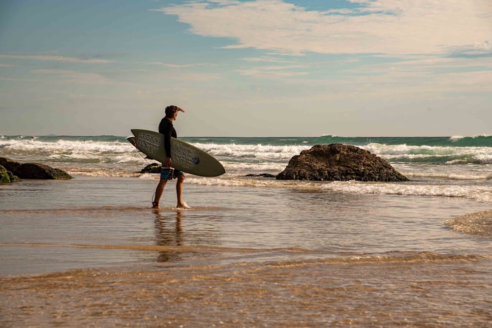 man holding white surfboard standing on seashore during daytime