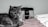 A grey tabby cat lies on a white and red striped fabric, next to a stylish Prada handbag with a black strap and metal detailing. The relaxed pose of the cat and the elegant design of the handbag create a blend of casual comfort and sophistication.