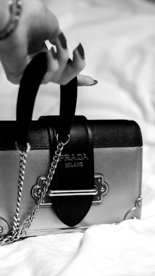 Black and white close-up of a sleek leather handbag with fine stitching details on a minimalist background