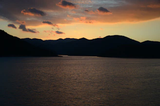 Sunset view over the turquoise waters of Kolsay Lake framed by lush green mountains.
