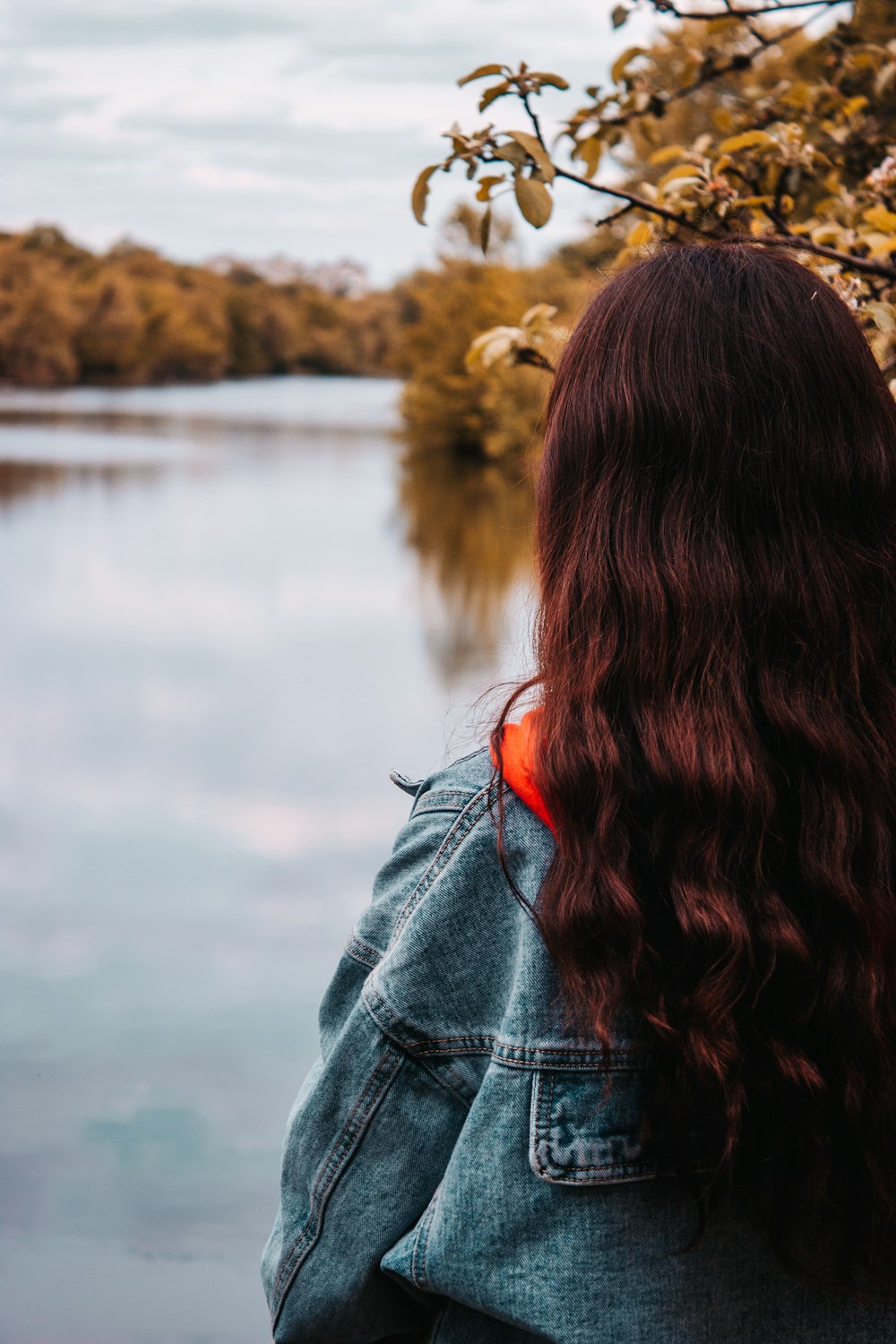 woman in blue denim jacket standing near body of water during daytime