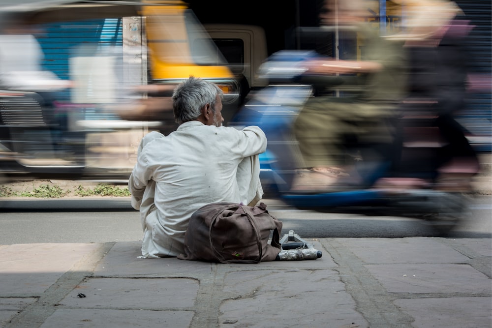 man in white hoodie sitting on sidewalk during daytime