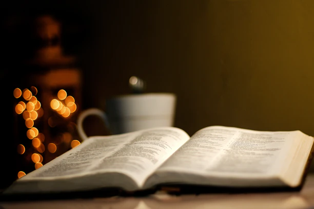 A warm, softly lit open Bible beside an antique lantern on a rustic wooden table.