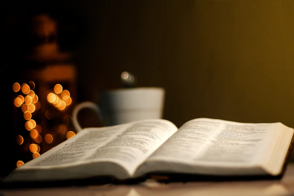 A cozy, softly lit room with an open Bible resting on a wooden table beside a steaming cup of tea.