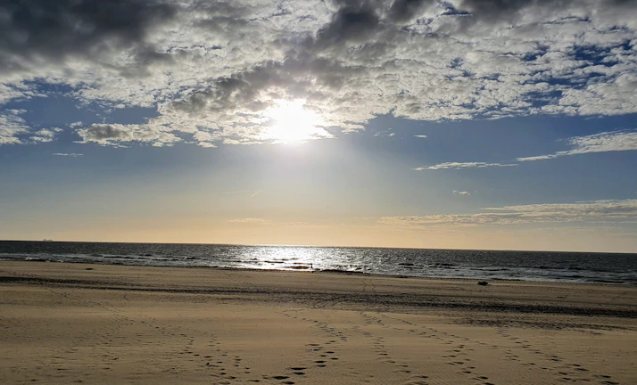 A serene beach with turquoise water and footprints in the sand at dawn.