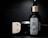 A bottle of beard oil with a silver dropper cap is displayed prominently. The label features an illustration of a bearded man and branding details. Beside it, a metallic clipper head is partially visible against a dark background.