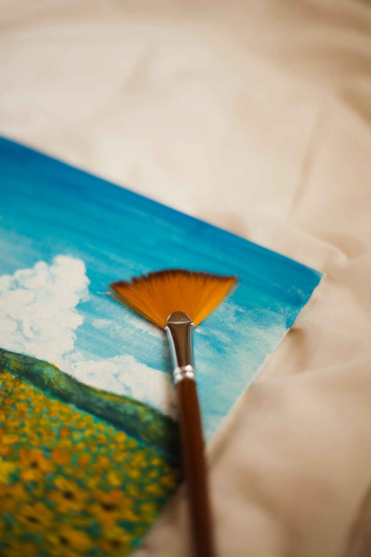 A small painting of a flower field under a cloudy sky, with a fan brush