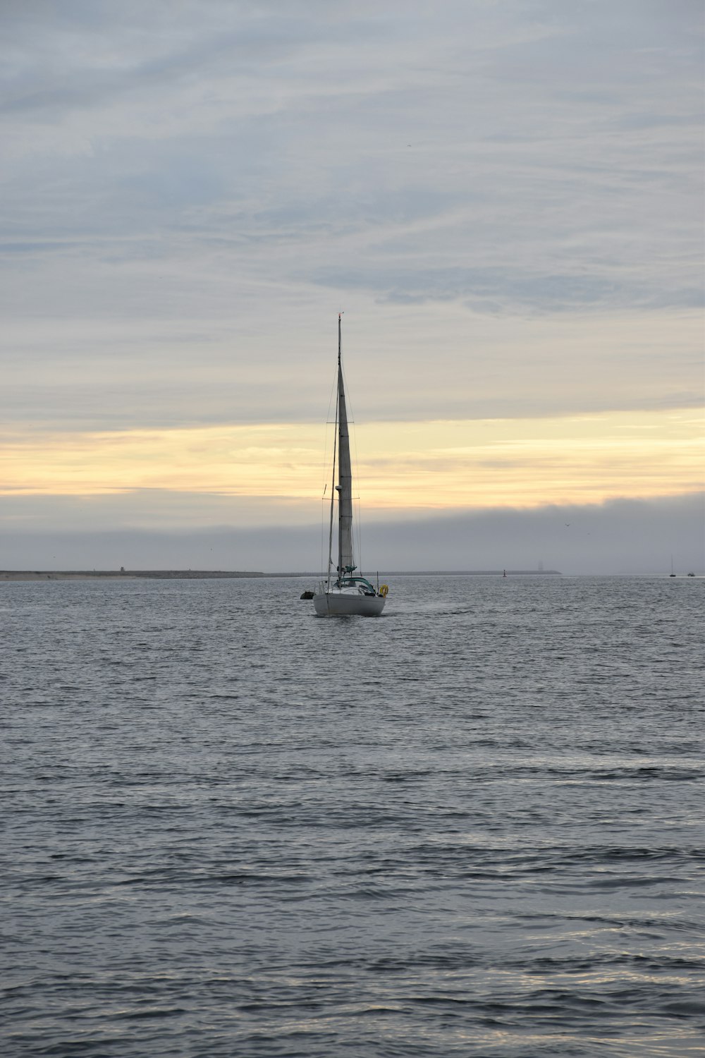 夕暮れ時の海上の白い帆船