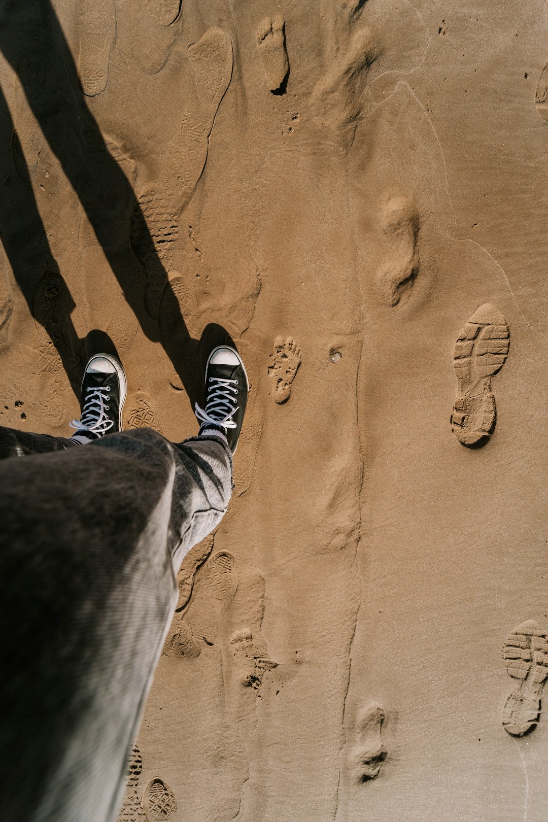 person in black pants and black and white sneakers standing on brown sand