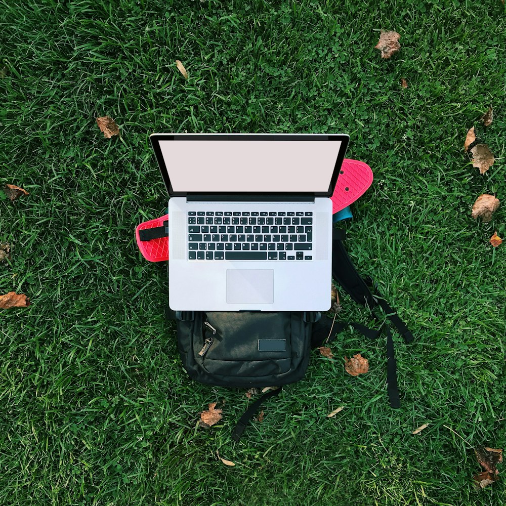 macbook air on black backpack on green grass