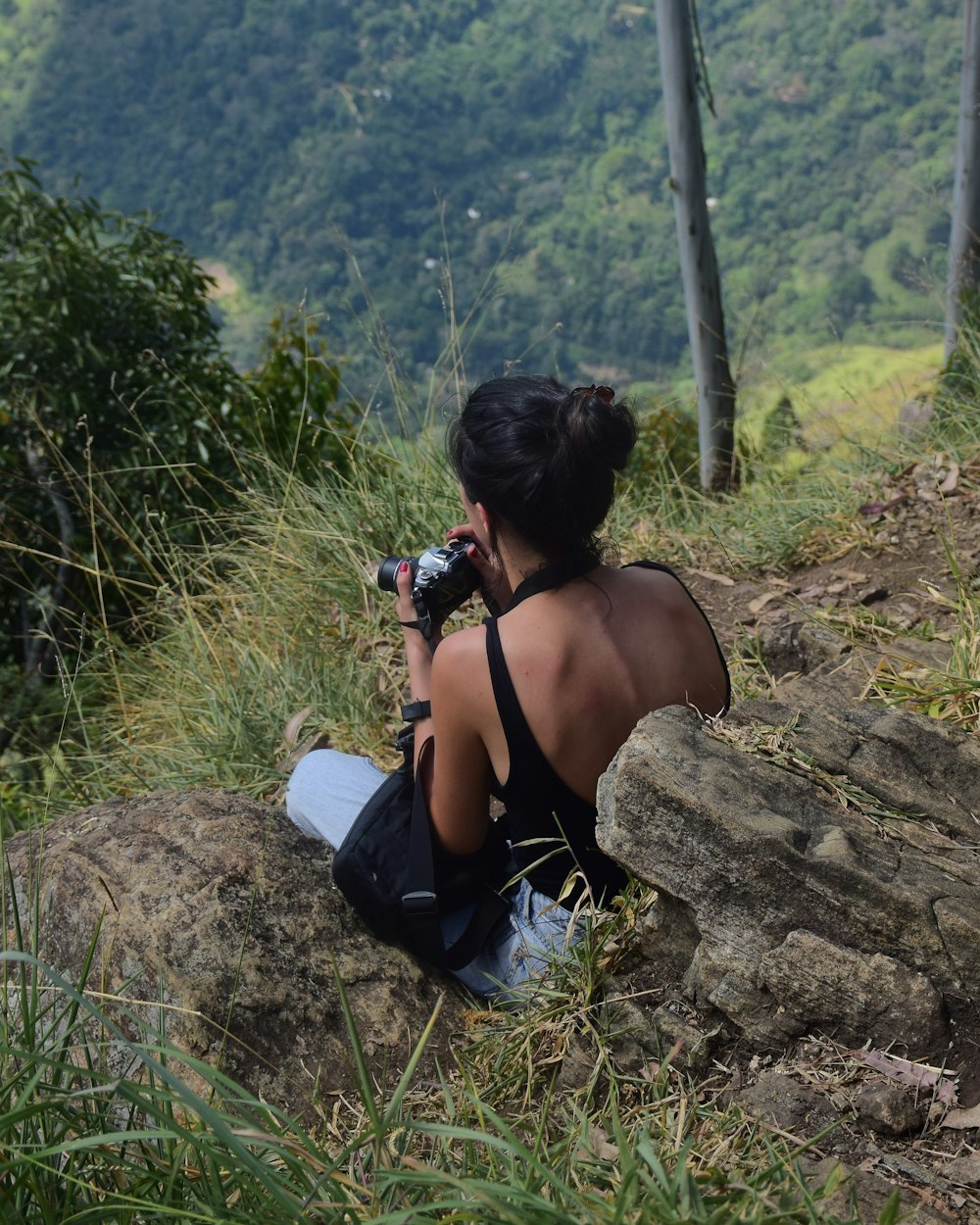 woman in black tank top and black pants sitting on rock during daytime