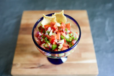 A vibrant salsa bowl surrounded by fresh tomatoes, peppers, and a baseball bat resting nearby.