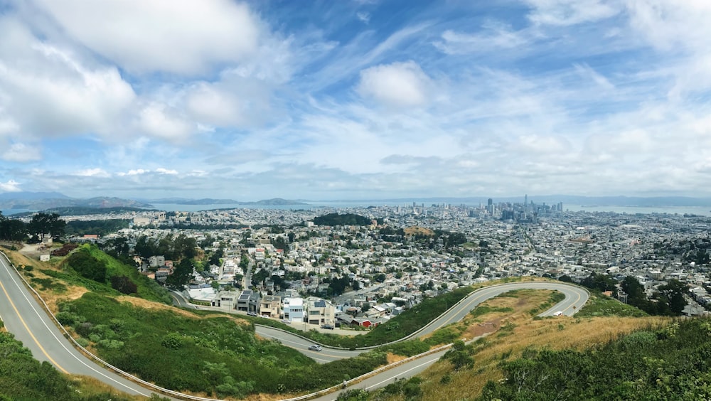 aerial view of city buildings and green grass field under blue and white sunny cloudy sky